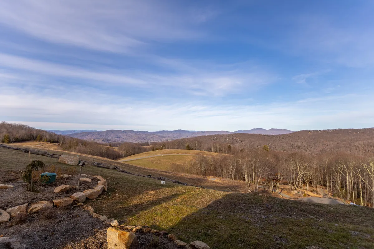 A sweeping outdoor view featuring distant mountains, expansive open fields, bare trees, and rugged rock formations. The atmosphere is tranquil, and the wide-open spaces evoke a sense of freedom and connection to nature.