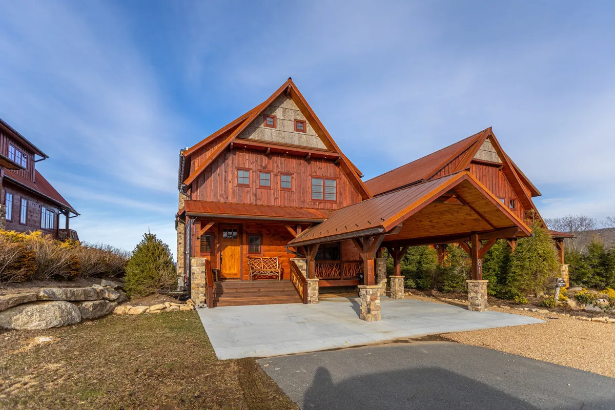 The hero image shows the inviting wooden facade of Whitetail Ridge Lodge, accented by sturdy stone pillars, a spacious covered porch, and a charming sloped roof. The porch overlooks sweeping mountain vistas, hinting at breathtaking sunset views and tranquil mornings with coffee in hand. The surrounding natural landscape offers a peaceful retreat, ideal for gatherings and relaxation.