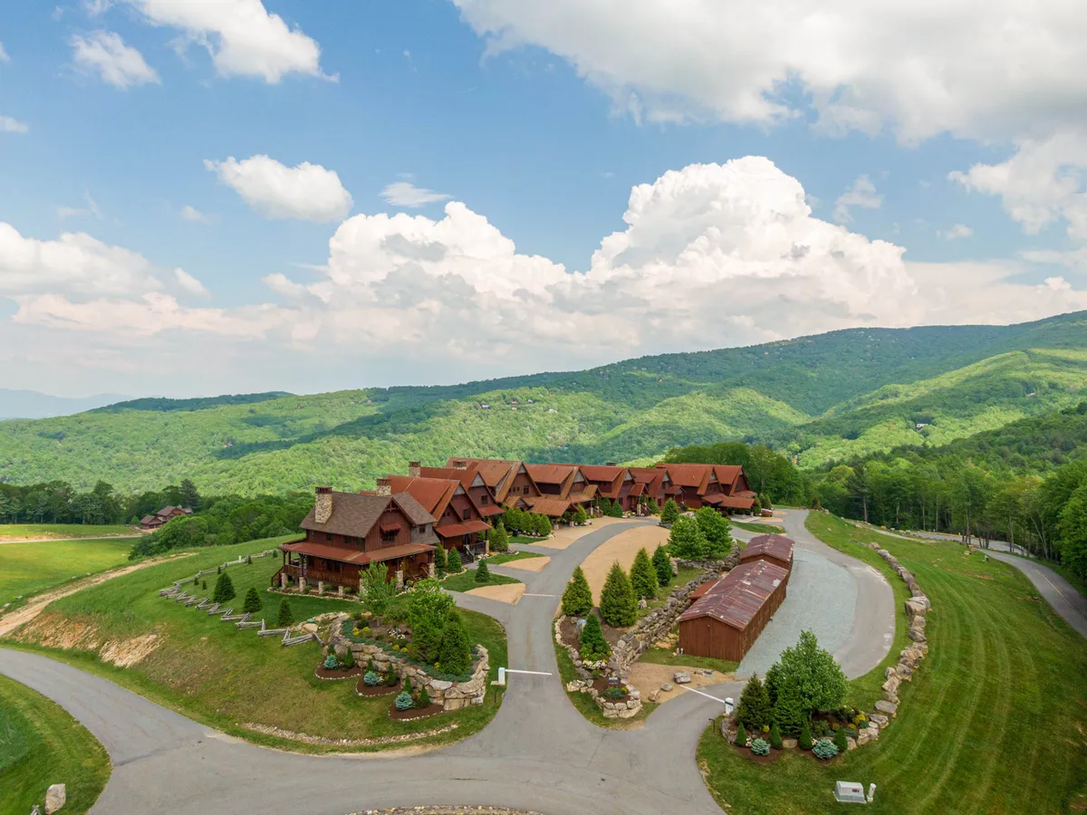 A wide exterior shot of lodge-style buildings surrounded by manicured lawns, with a mountain backdrop and open sky. The setting suggests group gatherings, family reunions, and a welcoming atmosphere for outdoor fun and scenic enjoyment.