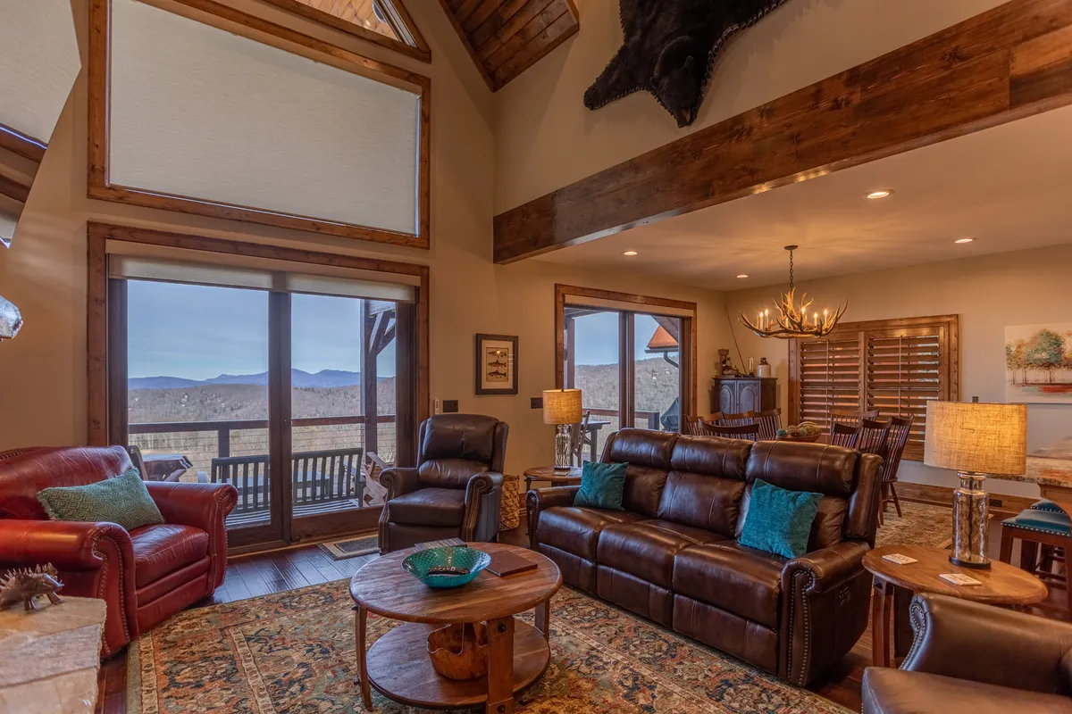 An inviting interior space featuring large windows that frame sweeping mountain views, rustic furnishings, and an antler chandelier. The space exudes warmth and offers an intimate vantage point for couples to relax and enjoy the landscape from indoors.