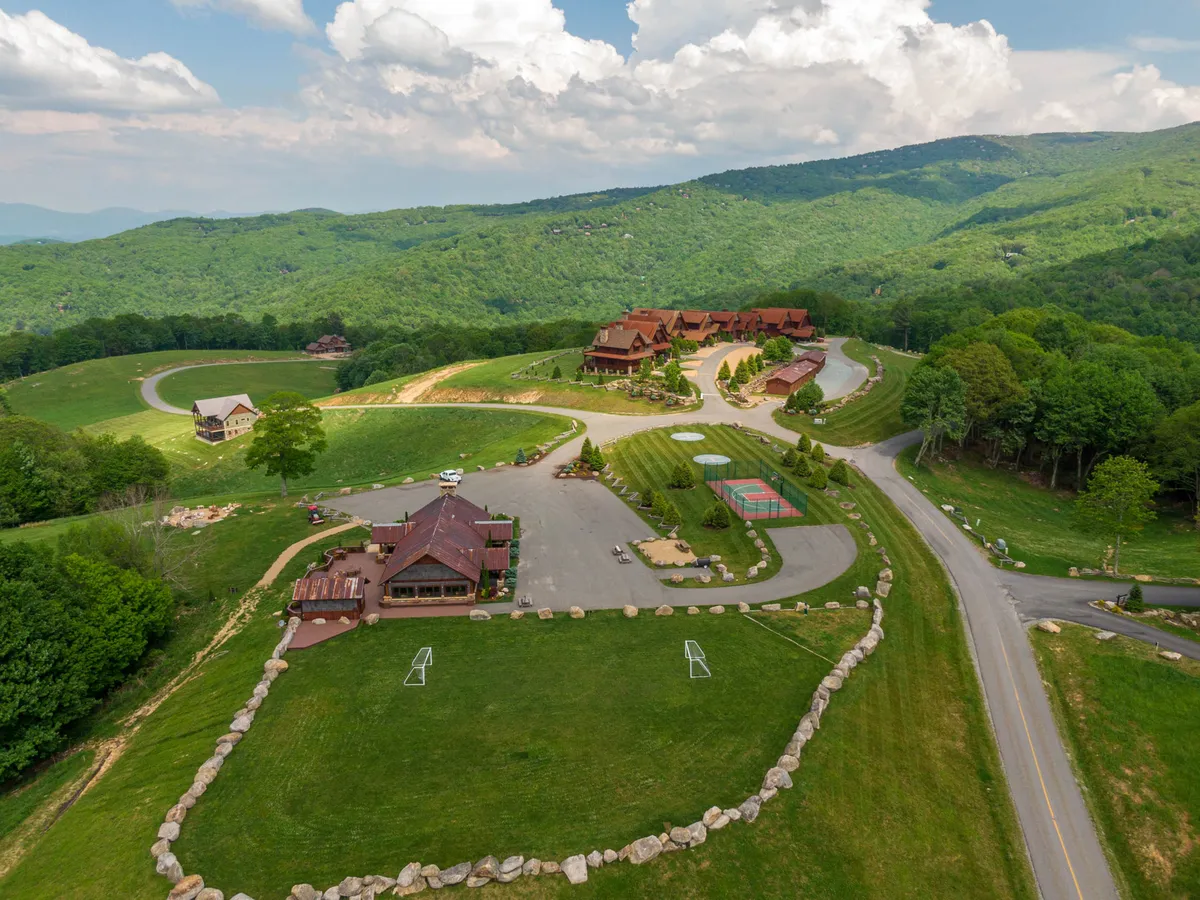 A panoramic view of green fields dotted with lodges nestled in the hills, leading to a basketball court and well-maintained walking paths. The serene setting highlights both the recreational opportunities and the tranquil, resort-like environment.