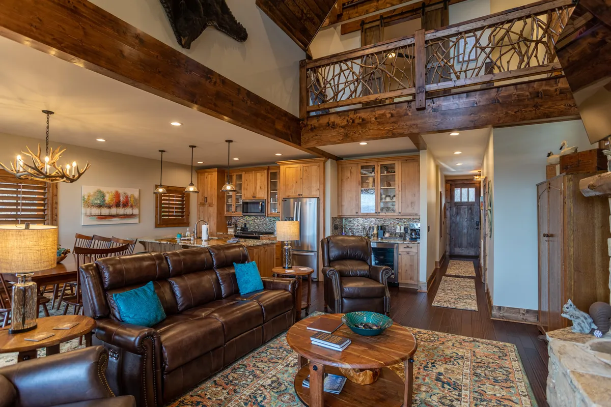 A cozy interior scene with a leather sofa and wooden dining table set beneath a chandelier, with the warm woodwork of a loft rail above. The space is perfect for relaxing after a day of adventure, gathering with loved ones, or enjoying quiet evenings.