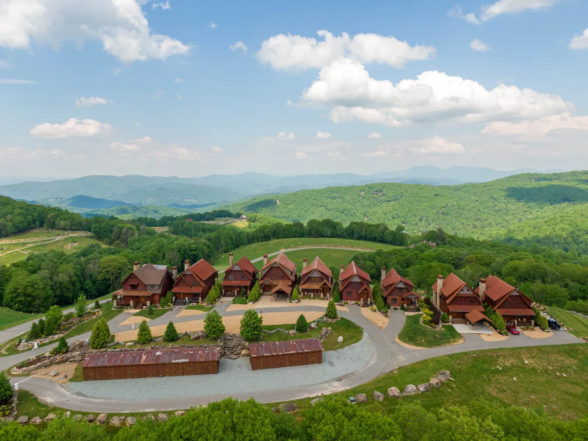 A row of rustic chalets sits nestled among lush green hills under a clear blue sky, exuding a sense of community and togetherness. The communal atmosphere and expansive surroundings invite outdoor gatherings and exploration, capturing the spirit of seasonal festivals and group celebrations.