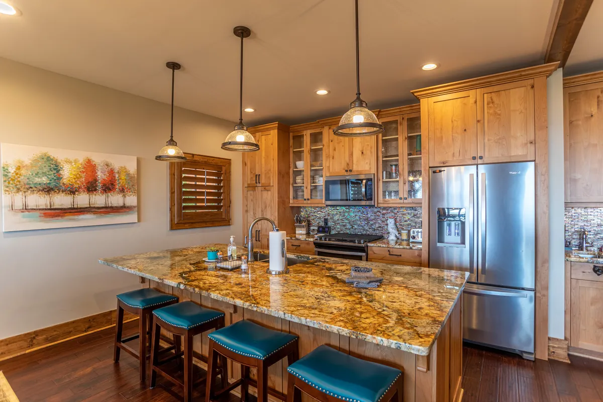 This image zooms in on the well-appointed kitchen, featuring a large kitchen island with a granite countertop, rich wood cabinetry, and colorful wall art accents. The scene suggests a space for meal preparation, entertaining, and casual dining, reinforcing the quality finishes and social aspect of the kitchen.