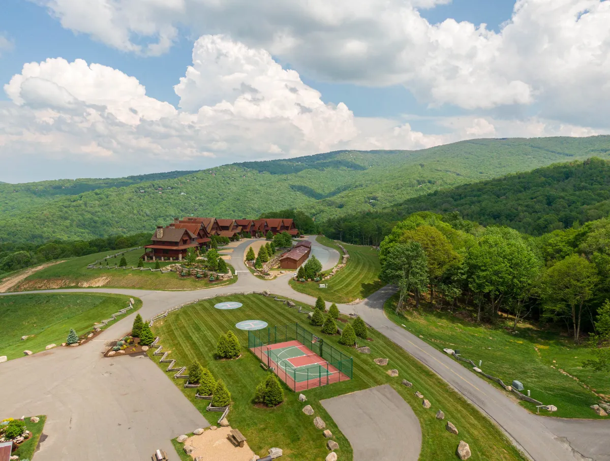 An exterior view featuring mountains, lodge-style buildings, a tennis court, and manicured lawns. The scene is lively yet serene, suggesting multiple outdoor activities (tennis, hiking, gatherings) in a stunning natural setting.
