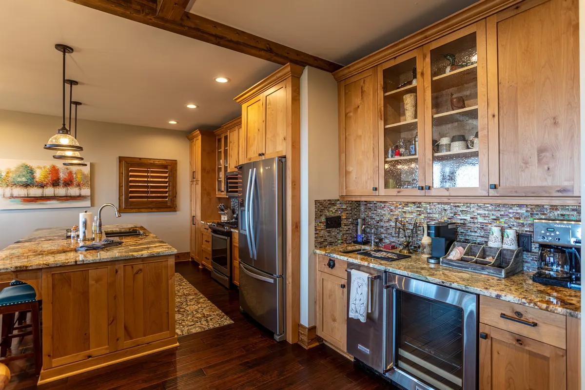 The image features a well-equipped kitchen with granite countertops, warm wooden cabinetry, stainless steel appliances, and a colorful tile backsplash. The space is lively and welcoming, designed for cooking, socializing, and hosting memorable family gatherings after active days outdoors.